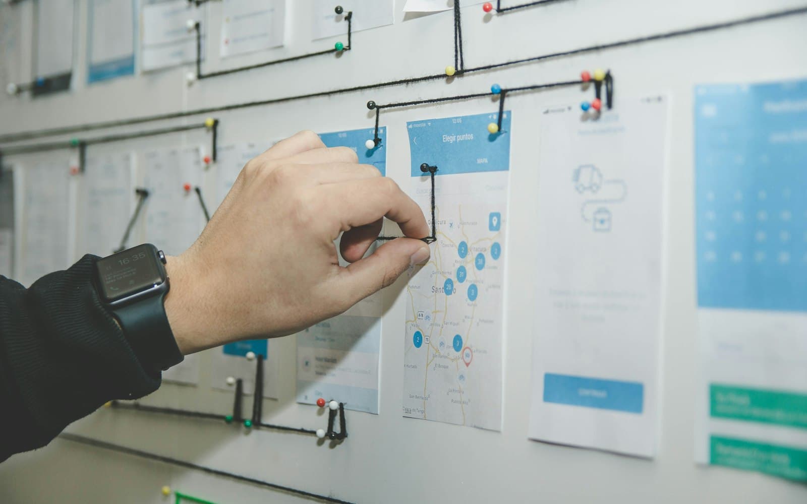 Hand arranging screen wireframes pinned to a whiteboard
