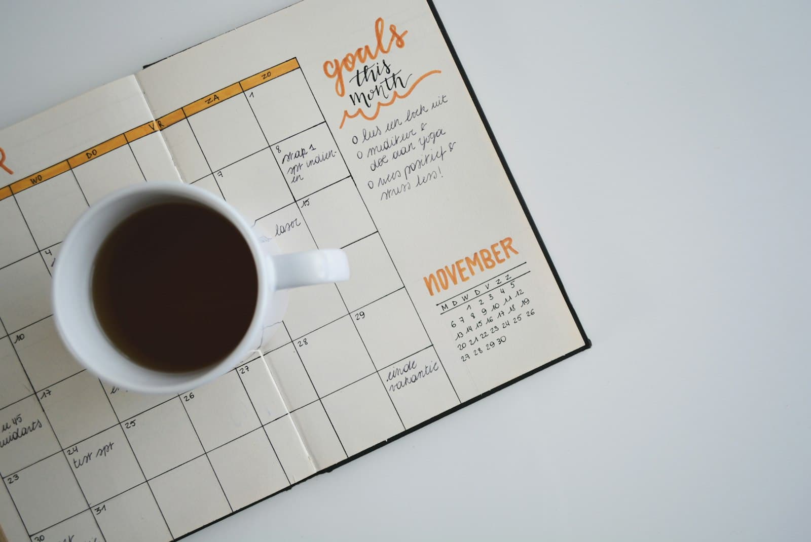 A monthly planner open on a desk beside a cup of coffee
